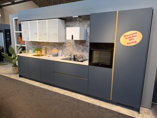 Strakke wandopstelling in het Fjordblauw, gecombineerd met glas-bovenkasten en gouden accessoires.