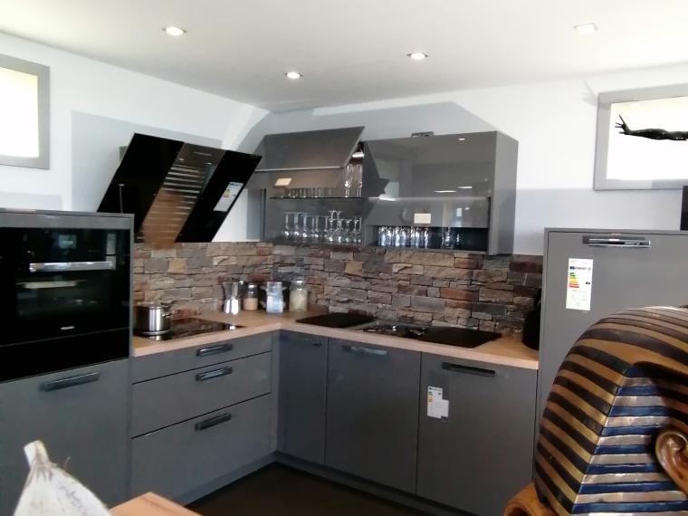 Modern - elegant - gradlinig. Anthrazitfarbene Küche in Lackausführung mit heller Arbeitsplatte in Holz-Optik und Nischenrückwand in Naturstein-Optik