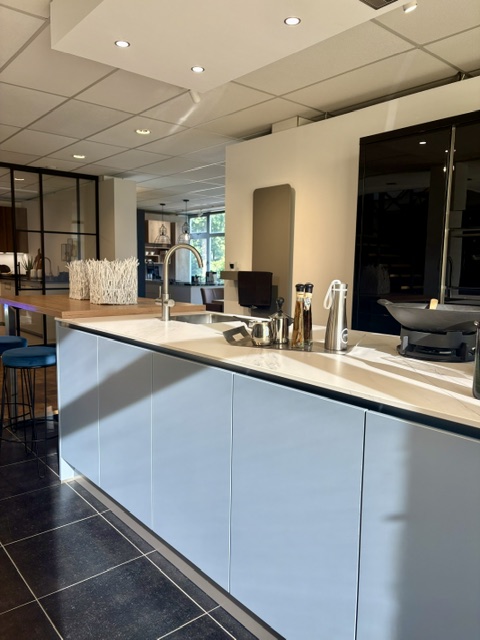 Moderne keuken met een lichtblauw eiland en keramiek marmer look blad, gecombineerd met zwarte hoogglans kasten