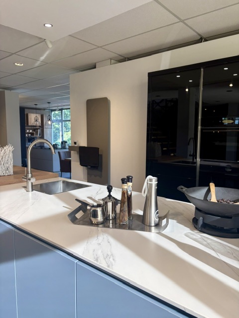 Moderne keuken met een lichtblauw eiland en keramiek marmer look blad, gecombineerd met zwarte hoogglans kasten